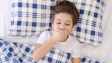 Hasta çocuk boynuna dokunuyor, boğaz ağrısı ve grip, boğaz enfeksiyonu. Küçük çocuk yatakta uzanıyor ve evdeki kağıt mendile burnunu siliyor. Alerji, grip.