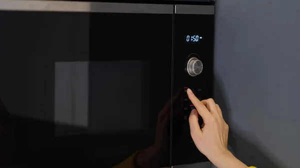 Mujer manos calentando un recipiente de comida en el horno de microondas moderno para el almuerzo de aperitivos en casa — Foto de Stock