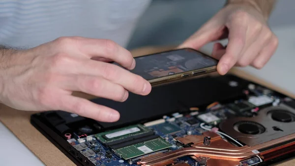 Nierozpoznawalny inżynier robi zdjęcia płyty głównej laptopa na smartfonie. Remont elektroniczny, biznes, koncepcja zawodu — Zdjęcie stockowe