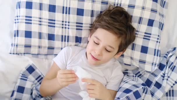 Dětská chřipková tkáň vysmrkající se do nosu. batole chlapec leží v posteli a fouká nos do hedvábného papíru doma. Alergie, chřipka — Stock video