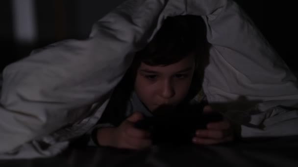 Een jongen die in het donker aan de telefoon speelt. Langdurig telefoneren heeft negatieve gevolgen voor het gezichtsvermogen en de gezondheid van jonge kinderen. Afhankelijkheid van een mobiele telefoon. — Stockvideo