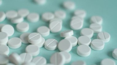 Beyaz haplar yavaş çekimde mavi arka plana düşüyor. Tabletler havada uçuşuyor. Tıbbi görüntüler, sağlıklı yaşam tarzı, vitaminler, ilaçlar.