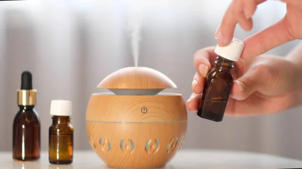 Moderner Aromaöldiffusor auf dem weißen Tisch. Spa-Konzept für Körper und Gesundheit. Weibchen fügt ätherisches Öl zu einem Aromadiffusor hinzu. lizenzfreie Stockbilder