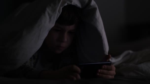 Een jongen die in het donker aan de telefoon speelt. Langdurig telefoneren heeft negatieve gevolgen voor het gezichtsvermogen en de gezondheid van jonge kinderen. Afhankelijkheid van een mobiele telefoon. — Stockvideo