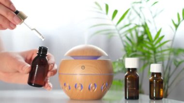 Beyaz masada modern aroma yağı yayıcısı. Vücut ve sağlık için spa konsepti. Dişi, aroma difüzörüne gerekli yağı ekliyor..