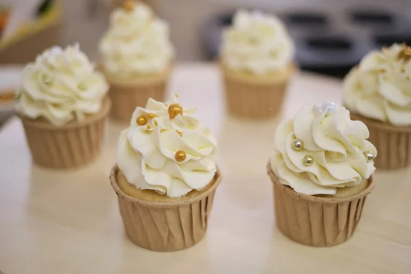 Bolinhos saborosos em tábua de madeira. Decorar um bolo branco com creme do saco de pastelaria. — Fotografia de Stock