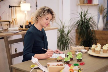 Kadın rahat mutfakta kek yaparken notlar yazıyor. Hobi olarak yemek pişirmek, pasta şefi için yüksek lisans yapmak..