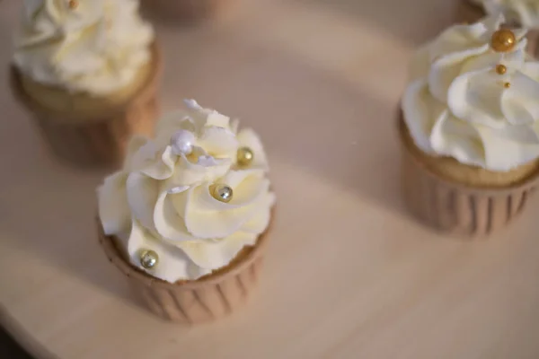 Bolinhos saborosos em tábua de madeira. Decorar um bolo branco com creme do saco de pastelaria. — Fotografia de Stock