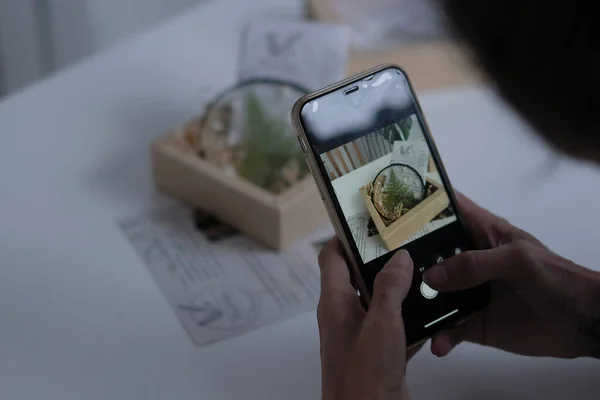Kunsthandwerker fotografiert ihre Handarbeit mit ihrem Smartphone, um sie zum Verkauf ins Internet zu stellen. Stockbild
