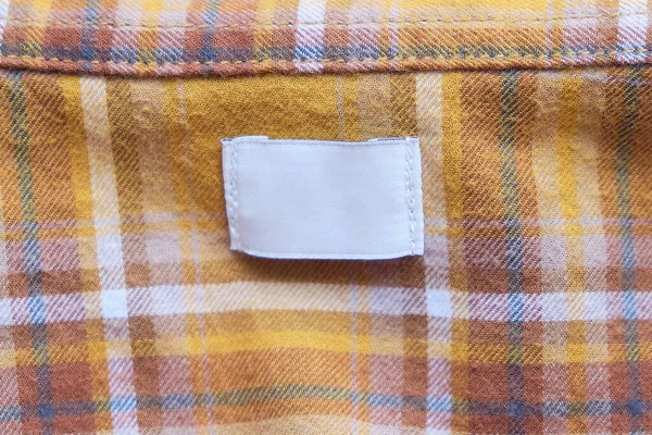 Etiqueta de ropa blanca en blanco para el cuidado de la ropa sobre tela amarilla textura fondo. — Foto de Stock