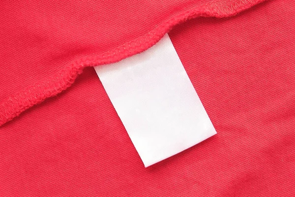 Etiqueta de ropa blanca en blanco para el cuidado de la ropa en tela roja textura fondo. — Foto de Stock