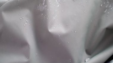 Yavaş Hareketli Su Çekimi su geçirmez kumaşa sıçrıyor. Kumaşta boncuk boncuk su. Su damlalarıyla su geçirmez kaplama. Yumuşak odaklı, bulanık