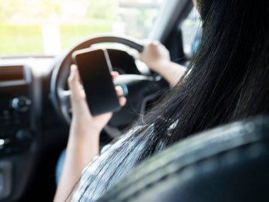 Direksiyon başında araba kullanırken telefon kullanan bir kadın modeli. Aracın içinde yakın plan akıllı telefon, direksiyon ve siyah iç mekan, kadın sürücü kavramı