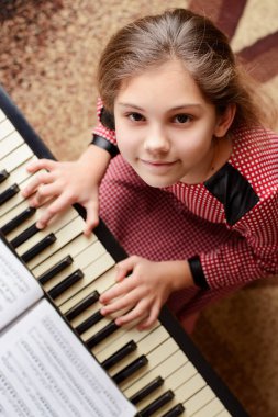 Kırmızı elbiseli küçük mutlu bir piyanistin portresi piyanonun başında oturmuş klasik müzik eşliğinde kameraya gülümsüyor.