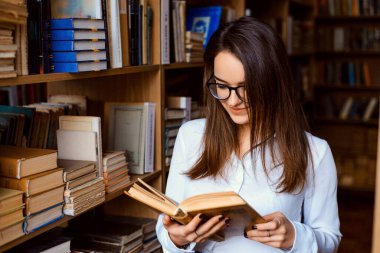Genç çekici üniversite öğrencisi kütüphanede kitap okuyor.