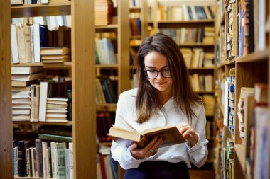 Kütüphanede kitap okuyan, araştırma yapmak için malzeme arayan bir kız öğrenci.