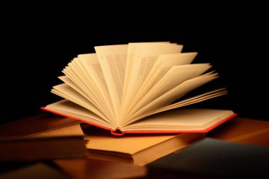 Masanın üzerinde kırmızı açık bir kitap ve kitabın açık sayfalarına ışık huzmesi gelen diğer kapalı kitaplar var.