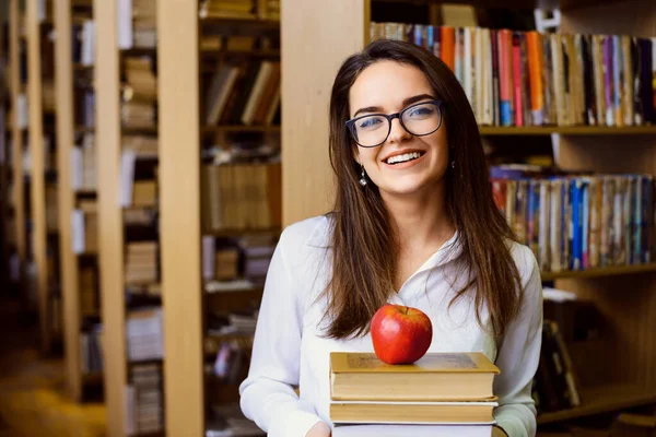 Happy student with a lot of books and an apple in the library. Hard-working student likes studying