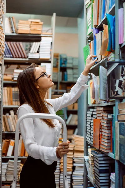 Junge Attraktive Bibliothekarin Steht Auf Der Leiter Und Überprüft Bücher — Stockfoto