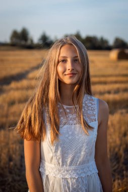 Gün batımında genç bir kızın güzel portresi. Yüzünde ılık sarı güneş ışınları ve arka planda saman balyaları var.