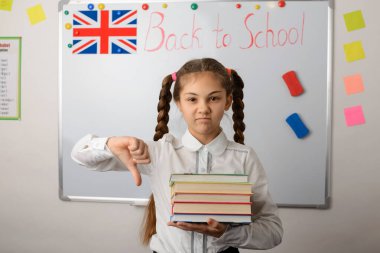 Hayal kırıklığına uğramış ve üzgün liseli kız koca parmağını gösteriyor, sınıfta duruyor çalışmaktan yoruluyor, eğitim görüyor.