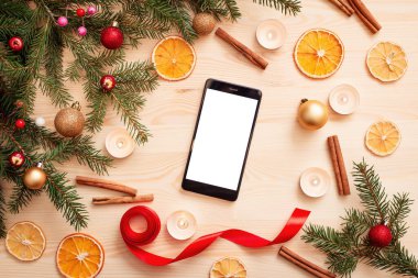 Masada parlak noel süslemeleri ve ortasında boş beyaz ekran olan cep telefonu. Noel kopyalama alanı