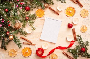 Tahta masanın üzerinde çeşitli noel süsleriyle çevrili boş bir defter. Yeni yıl havası, şenlikli kompozisyon, düz yatak.