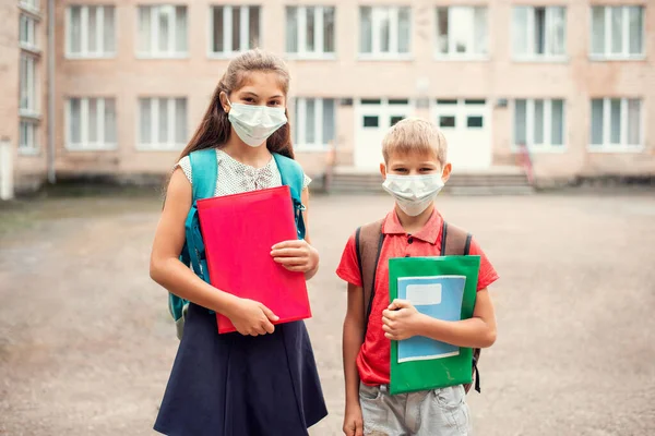 School learners of different age in front of conventional school in medical masks. Concept of education during the pandemic