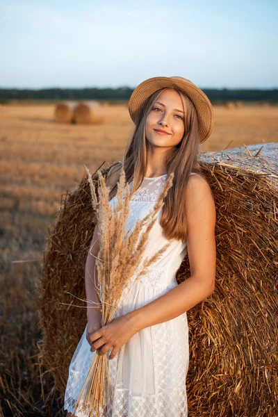 年轻的金发姑娘靠在稻草捆上 捧着一束干花 捕捉着夕阳西下的最后一丝温暖的阳光 — 图库照片