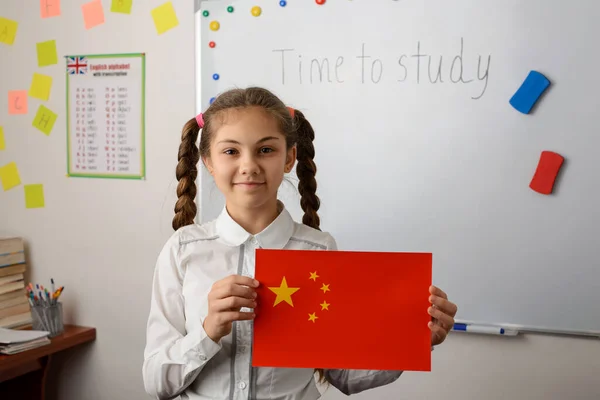 Cheerful schoolgirl showing flag of China in the classroom. Concept of studying chinese language