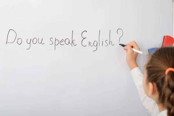 Concept of studying English. Schoolgirl writing inscription Do you speak English? on the whiteboard in the classroom