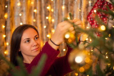 Kış tatilinden önce Noel ağacını süsleyen neşeli esmer kız. Sıcak çelenk ışığı, odadaki şenlikli atmosfer.