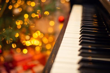 Arka planda parlak noel ışıkları olan piyano klavyesi. Dekore edilmiş arka planı olan eski bir piyanonun yakın plan çekimi.