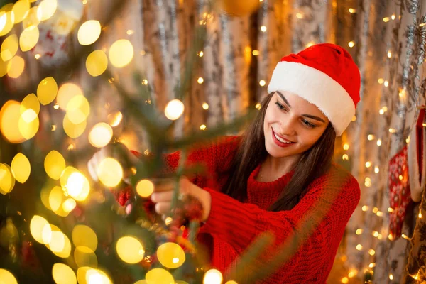 Noel ağacında parlak bir çelenk ışığı, kış tatilinden önce odayı dekore eden güzel bir genç kız. Kış zamanı, evde aile, mutlu bir ortam..