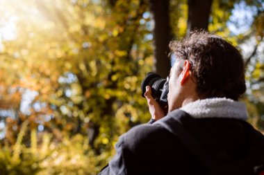 Fotoğrafçı, sonbahar ormanlarında parlak güneş ışığına karşı fotoğraf çekiyor.