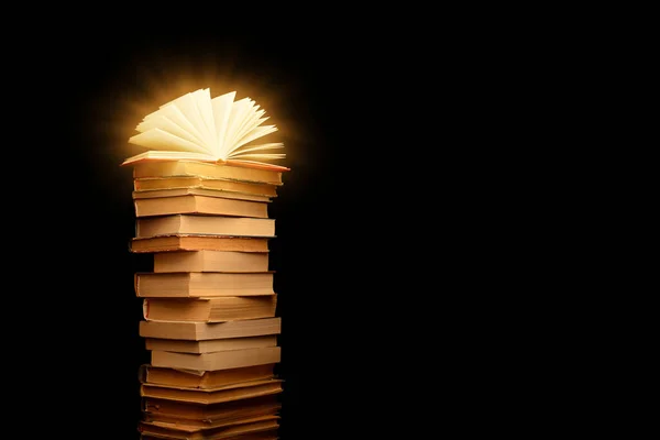 Stack of old books isolated on black background with open book and light coming from it`s pages