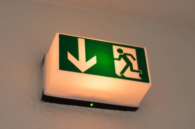 Yeşil parlayan bir binada acil çıkış işareti. İşaretin düzgün çalıştığını gösteren bir ok var