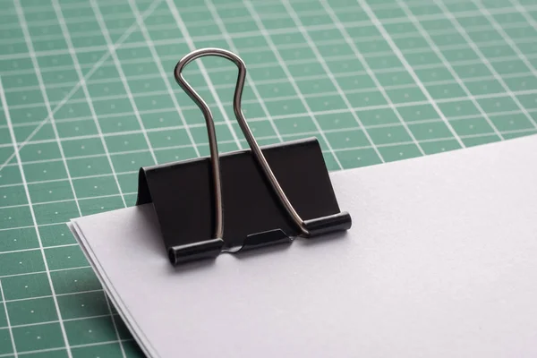 Big black paper clip on a pile of papers on a green cutting mat