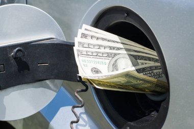 Amerikan doları banknotlarıyla dolu gümüş bir arabanın yakıt deposu, yüksek yakıt maliyetini simgeliyor.