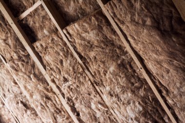 Özel bir evin tavanında, ahşap çerçeveli kahverengi cam yün. Evi fiberglasla ısıtıyor..