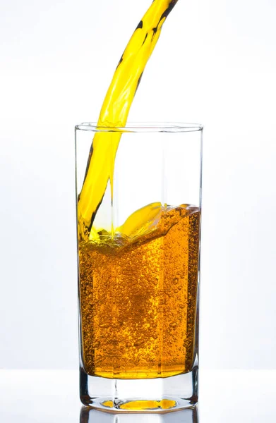 Pouring yellow juice in glass with bubbles