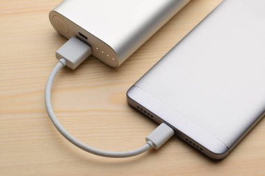 Gümüş akıllı telefon, elektrik bankasıyla birlikte, tahta arka planda şarj oluyor.
