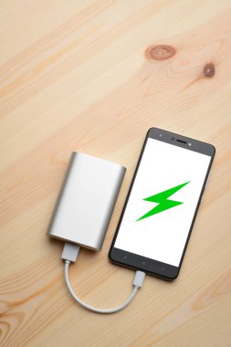 Telefon ahşap arka planda elektrik bankasıyla şarj ediliyor.