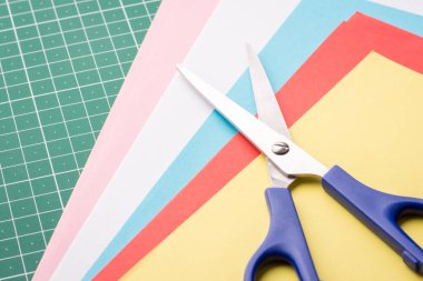 Makas ve kesme paspası üzerine renkli kağıtlar yığını