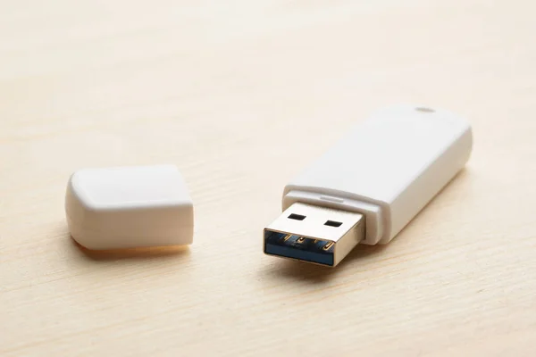 White unplugged USB stick with cap on a light wooden table