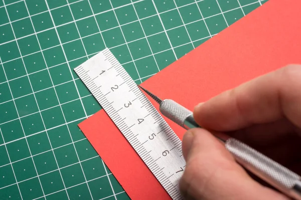 Male`s hand cutting red paper on cutting mat with scalpel and ruler