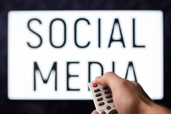 Male with remote controller switches off a TV set with inscription SOCIAL MEDIA on its screen