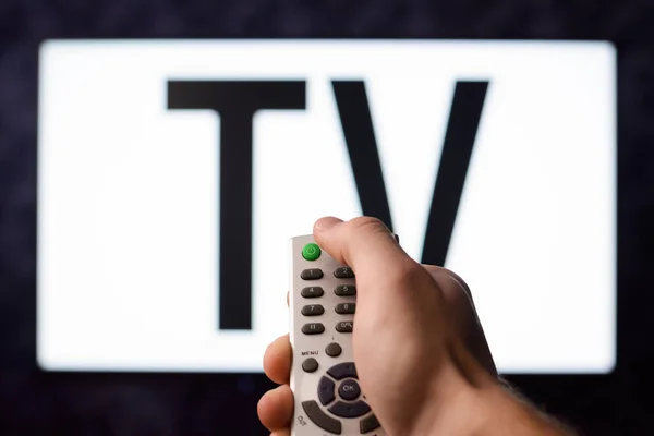 Male that interested in watching television turns on a modern TV set by pressing green button on a remote controller