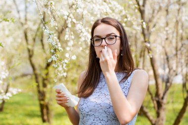 Sezonluk polenlere alerjisi olan, mendil ve burun spreyi kullanan, çiçek açan ağacın üzerine poz veren, rhinitis ve hapşıran genç bir kızın açık hava portresi. İnsanlar ve hastalık konsepti