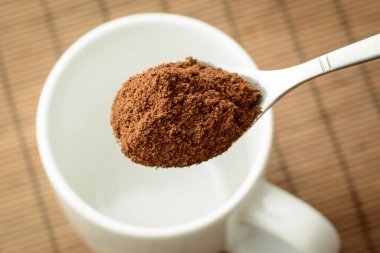 Kahverengi bambu arka planına karşı beyaz boş fincanın üzerinde öğütülmüş kahveyle kaşık. Kahve yapıyorum.